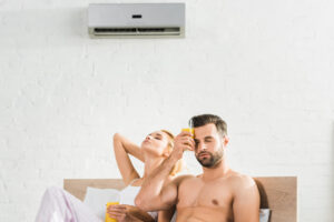 couple with orange juice suffering from heat under air conditioner in bed at home